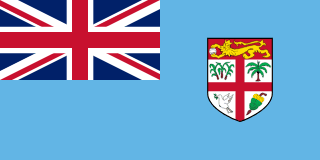 The flag of Fiji has a light blue field. It features the flag of the United Kingdom — the Union Jack — in the canton and the shield of the national coat of arms centered in the fly half.